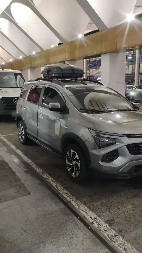 Carro cinza da Sameach, de lado, com o bagageiro no teto, no aeroporto